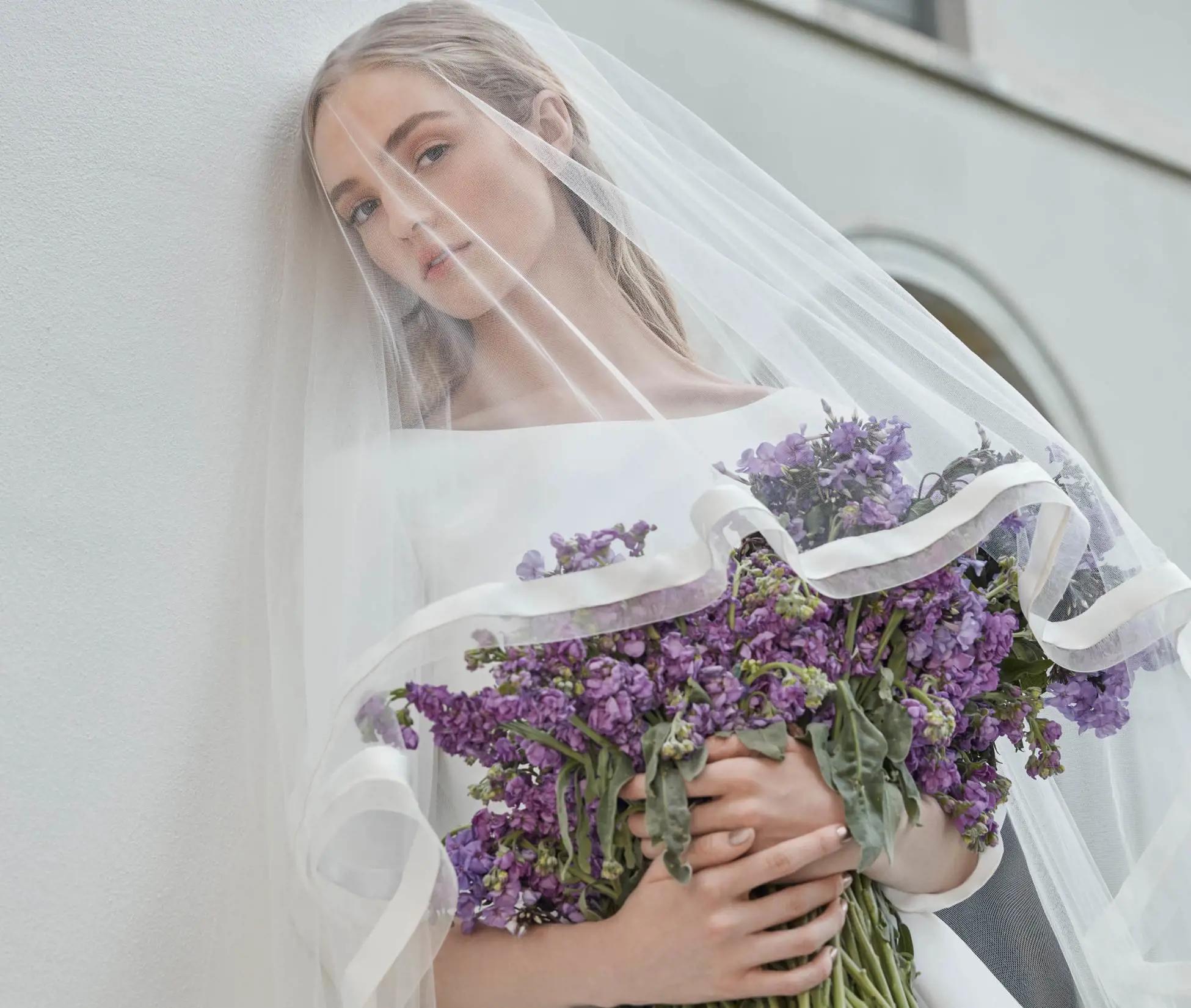 Bride with veil holding purple flowers wearing a gown from Sareh Nouri Fall 2022 collection
